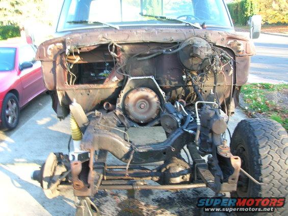 Truck chassis on jack stands, engine bay empty, transmission visible