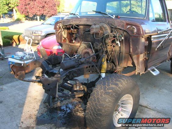 Brown 1970s Ford F-250 truck chassis with engine removed, jacked up, with other vehicles behind