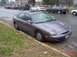 1996 Ford Taurus - A 1996 Ford Taurus is parked on a wet street, with other vehicles visible in the background.