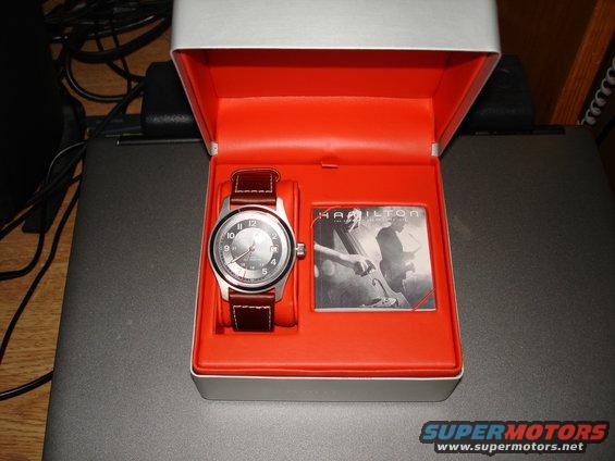 Hamilton watch with brown leather strap in an open orange-lined box next to a Hamilton card