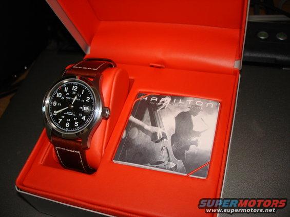 Hamilton watch with brown leather strap in an open orange box next to a booklet