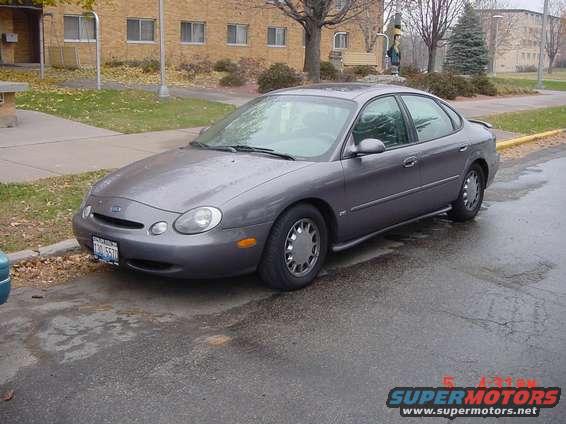 Gray 1996 Ford Taurus sedan parked on wet asphalt, front 3/4 view
