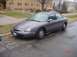 1996 Ford Taurus - A gray 1996 Ford Taurus sedan is parked on a wet street next to a sidewalk.