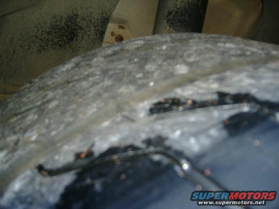Close-up of a dirty tire and part of a gray fender liner with some damage