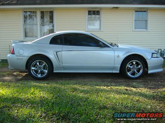 Silver Mustang parked in front of a house. It has aftermarket wheels and a spoiler