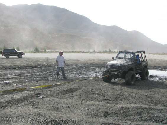 Suzuki Samurai stuck in mud, another SUV in background. Person standing between them