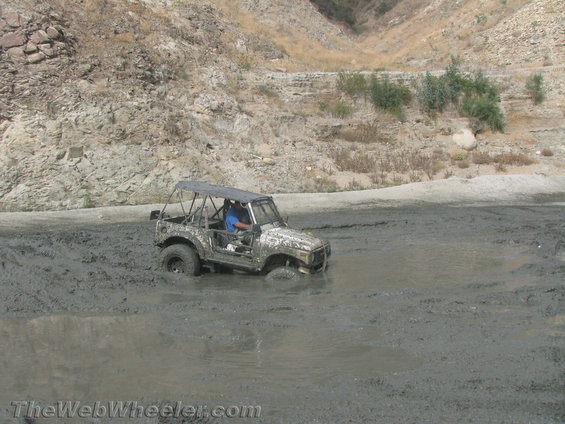 Suzuki Samurai stuck in mud pit, driver wearing blue shirt
