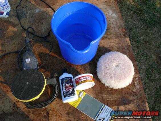 Car detailing supplies including a polisher, bucket, rubbing compound, and polishing pad on a rusty surface