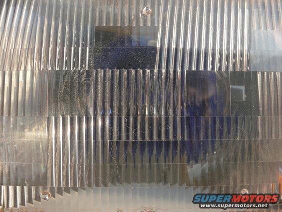 Close-up of a clear plastic headlight lens with horizontal and vertical fluting. Supermotors.net logo visible at bottom right