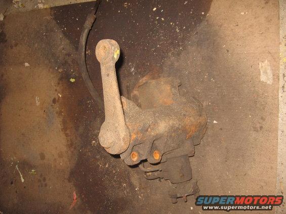 Rusty steering linkage component with a yellow-capped ball joint, on a dirty floor