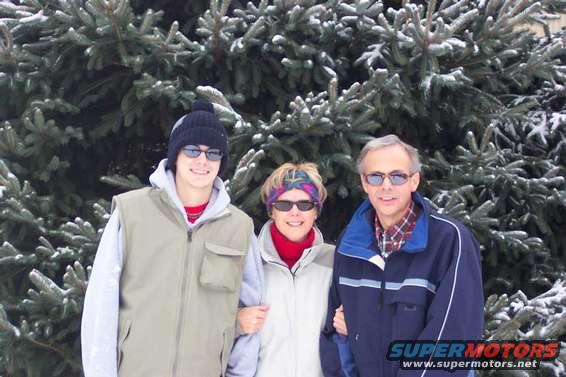 Three people stand in front of snow-covered pine trees