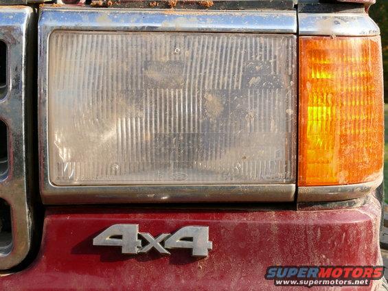 Red vehicle's front headlight and amber turn signal with chrome grille and 4x4 badge