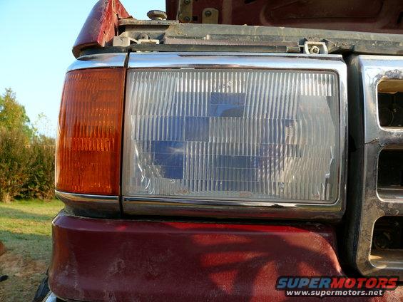 Red Ford truck's front headlight assembly with chrome trim and orange turn signal