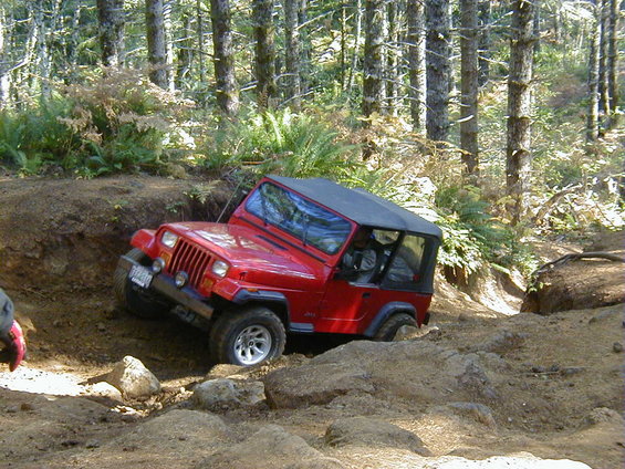 Red Jeep Wrangler navigating a steep dirt trail, front 3/4 view