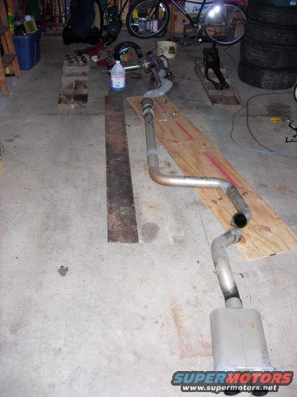 Exhaust system on a garage floor, with a bicycle and tires in the background