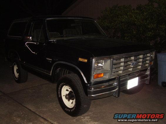 Black Ford Bronco parked at night, front 3/4 view. Chrome grille and bumper, white steel wheels
