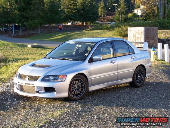 Silver sedan with a large rear spoiler and aggressive front bumper parked on gravel