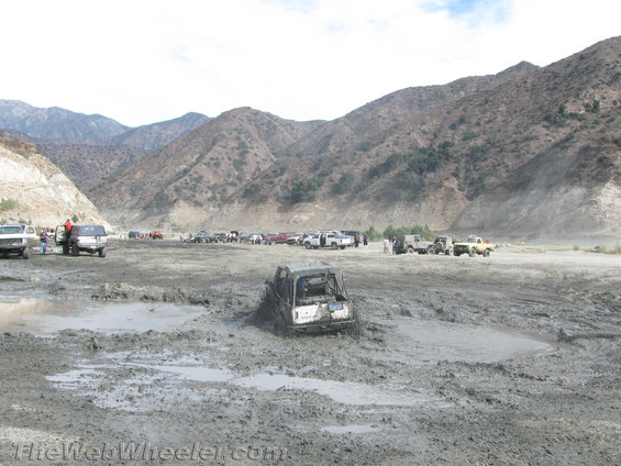Multiple off-road vehicles stuck in deep mud with mountains in the background