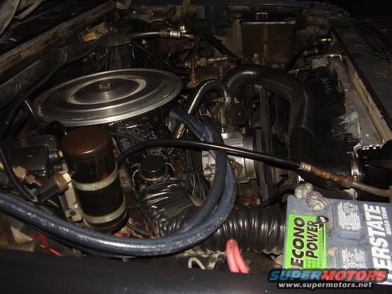 Engine bay showing air filter housing, hoses, battery, and engine components