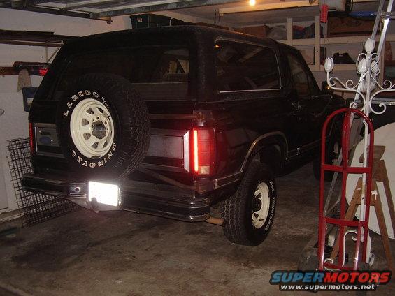 black SUV parked in garage, spare tire mounted on rear door, visible taillights and bumper