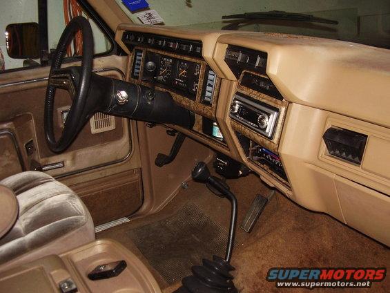 Tan interior of a 1980s truck with woodgrain trim, a four-spoke steering wheel, and a floor-mounted shifter