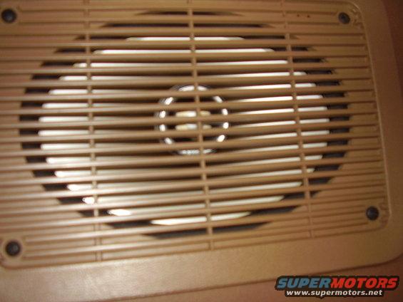Speaker grille with horizontal slats and a circular speaker visible behind it. Supermotors.net logo at bottom right