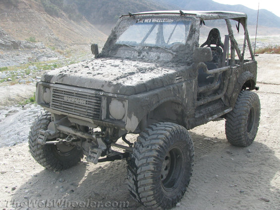 Mud-covered 1987 Suzuki Samurai with off-road tires and roll cage