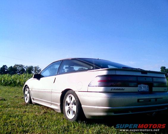 1990 Ford Probe GT parked in a grassy field with corn stalks and trees in the background