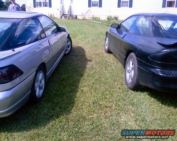 Two Ford Probe cars parked on grass in front of a house. One is silver, the other is black
