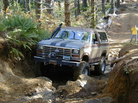 Ford Bronco with stripes on hood navigating a dirt trail, winch on front bumper