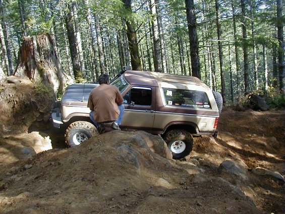 Brown and tan Ford Bronco II off-roading over dirt mounds, driver's side visible
