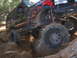 1989 Ford Bronco - Modified black SUV with flame decals climbs over rocks on a wooded trail.