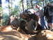 1989 Ford Bronco - An off-road vehicle navigates a challenging rocky terrain in a wooded area, with onlookers observing the ascent.