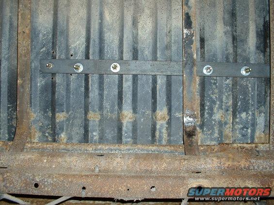 Corrugated metal panel with bolted metal strips, part of a vehicle's undercarriage