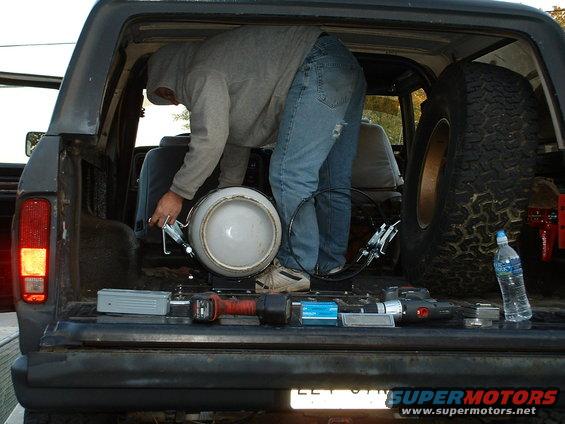 Person loading propane tank into back of SUV, spare tire visible