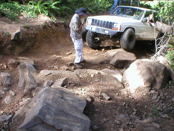 White Jeep Cherokee XJ on rocky trail, front 3/4 view, driver's side visible