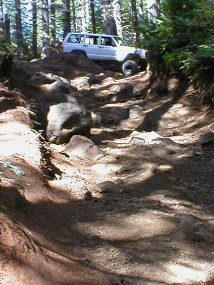 White Jeep Cherokee XJ driving on a rocky, wooded trail