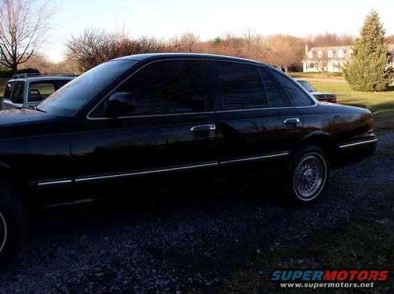 Side view of a black 1997 Ford Crown Victoria parked outside with another vehicle behind it