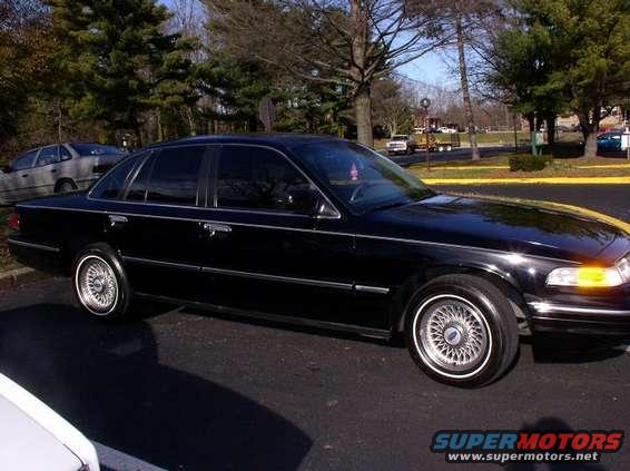 Black 1997 Ford Crown Victoria parked on asphalt, side view. Another car is visible behind it