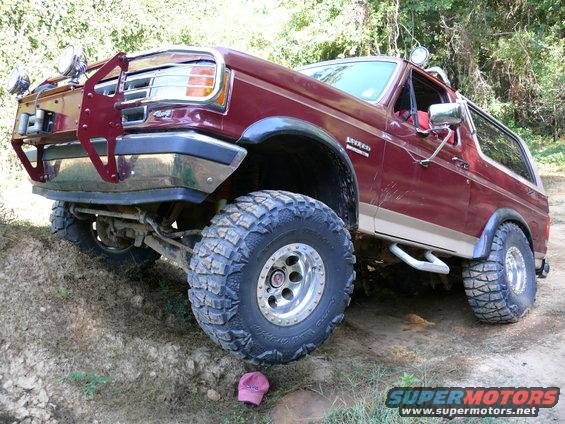Maroon Ford Bronco with off-road tires and a brush guard, angled on a dirt incline