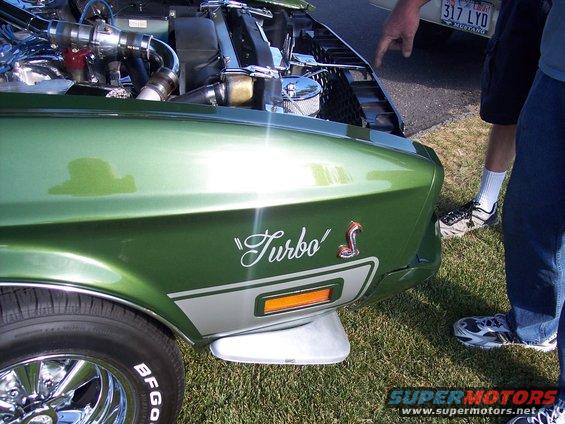 Green 1973 Ford Mustang fender with "Turbo" decal and snake emblem, chrome wheel, and part of engine visible