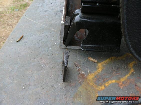 Close-up of a black seat bracket on a metal surface with a wedge and some debris