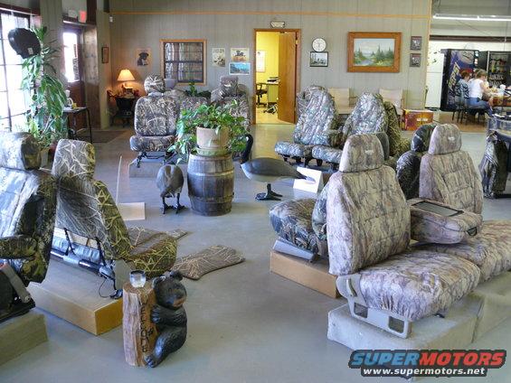 Multiple vehicle seats covered in camouflage fabric are displayed indoors