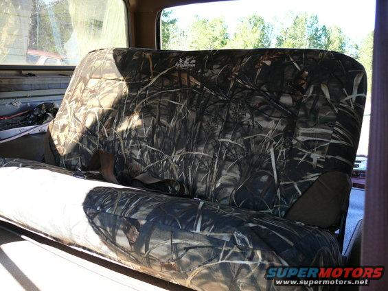 Interior shot of a vehicle's back seat with camouflage seat covers. A red vehicle is visible through the window