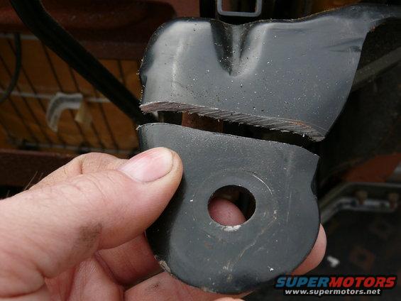 Hand holding a broken metal seat bracket with jagged edges. Seat fabric visible in background