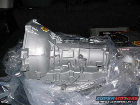 Silver transmission part in plastic wrap, with a yellow sticker and a box labeled 'TORQUE CONVERTER' in the background