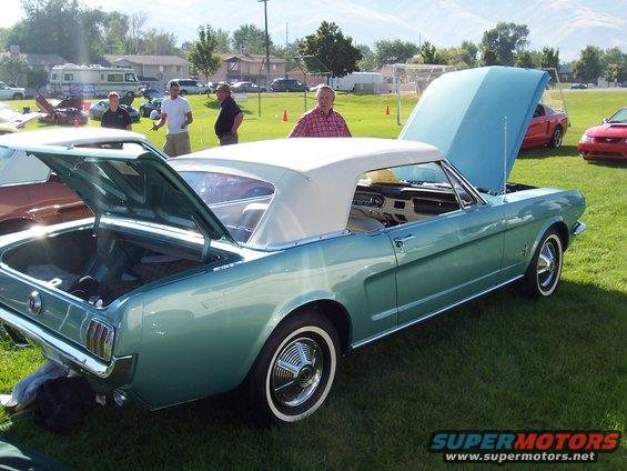 Teal convertible with white top and open trunk. Hood is also open. Other cars and people in background