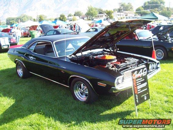 Black Dodge Challenger R/T with hood open, showing engine. Sign says 440 Six Pack. Other cars and tents in background