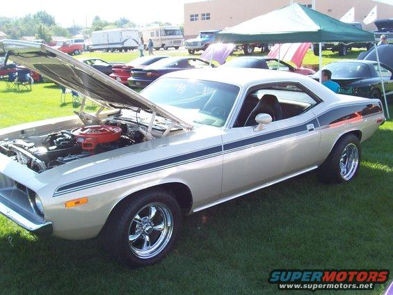 Gold 1970 Plymouth Barracuda with black racing stripes, hood open, on display