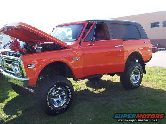 Orange lifted SUV with hood and driver door open. Chrome wheels and off-road tires visible